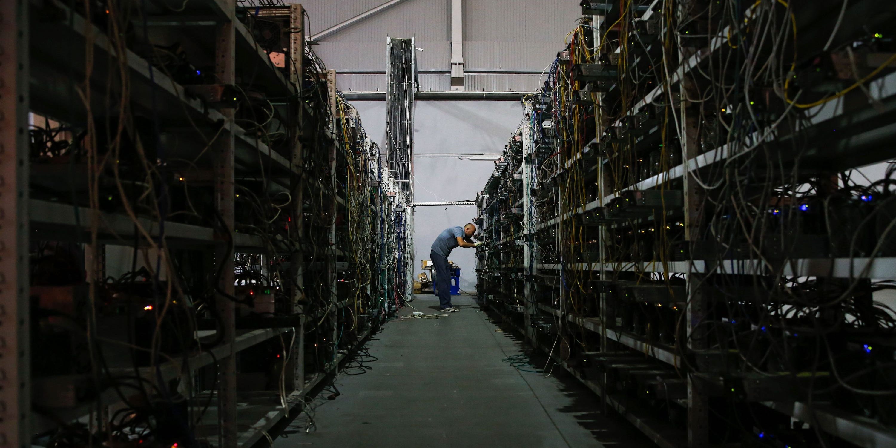 Un uomo si trova alla fine di un lungo corridoio. Le pareti sono piene di computer e cavi, che vengono utilizzati per estrarre bitcoin.