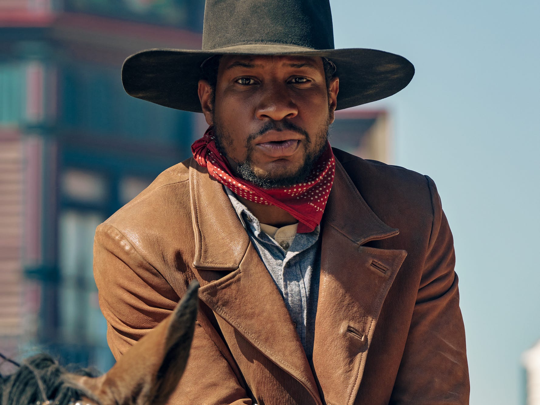 Un uomo (Jonathan Majors) siede su un cavallo che indossa una giacca di pelle marrone e un cappello da cowboy nero.