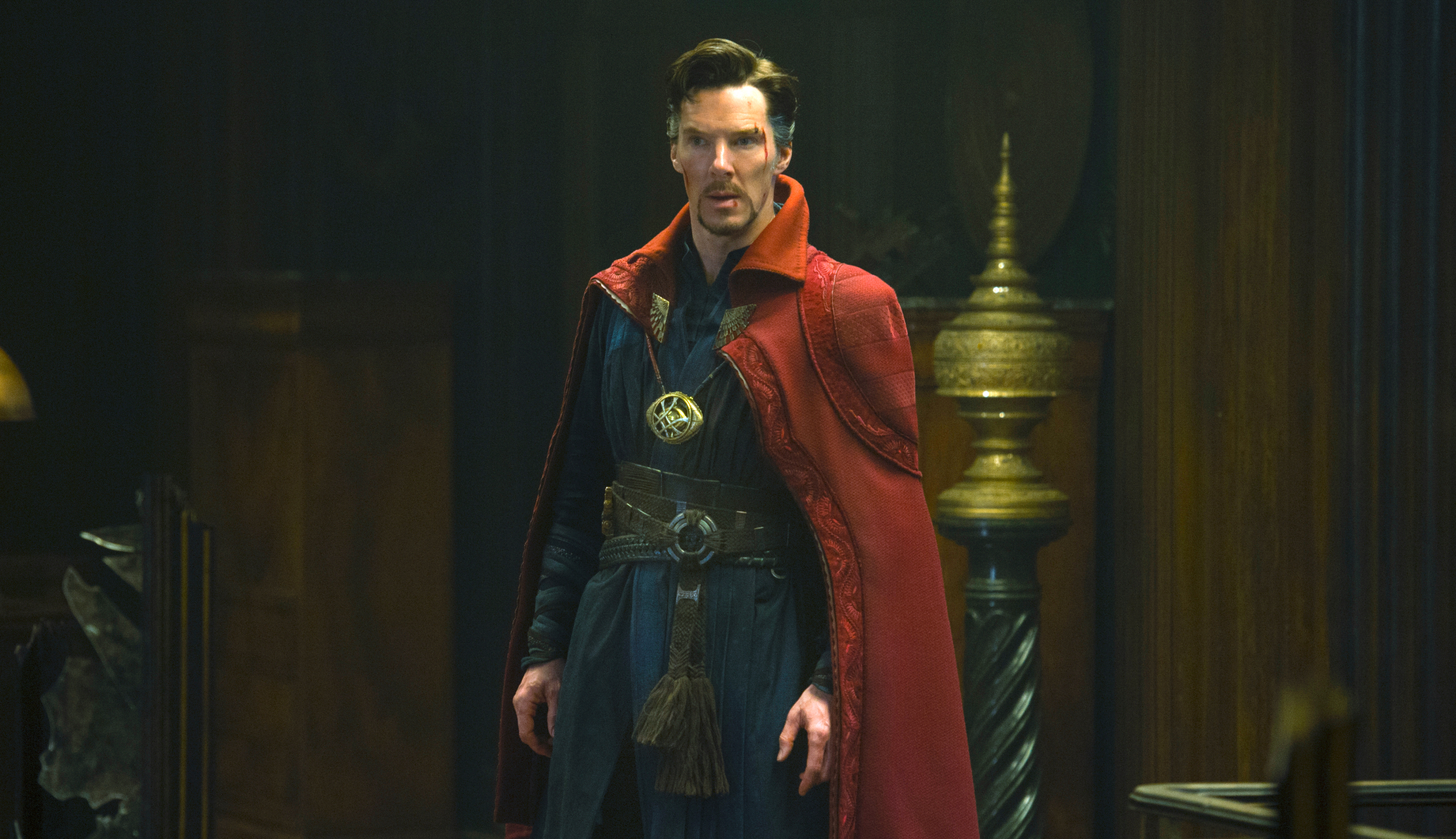 Il dottor Stephen Strange (Benedict Cumberbatch) in una stanza buia, con indosso il suo completo blu da supereroe e il caratteristico mantello rosso con colletto. La sua faccia presenta diversi tagli e graffi.